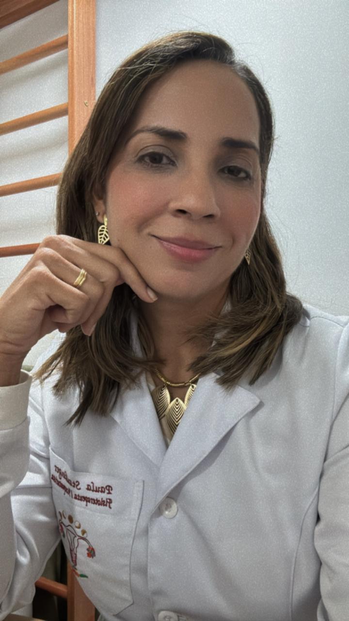 Dra. Paula Staudinger sorrindo, com a mão no queixo e jaleco branco